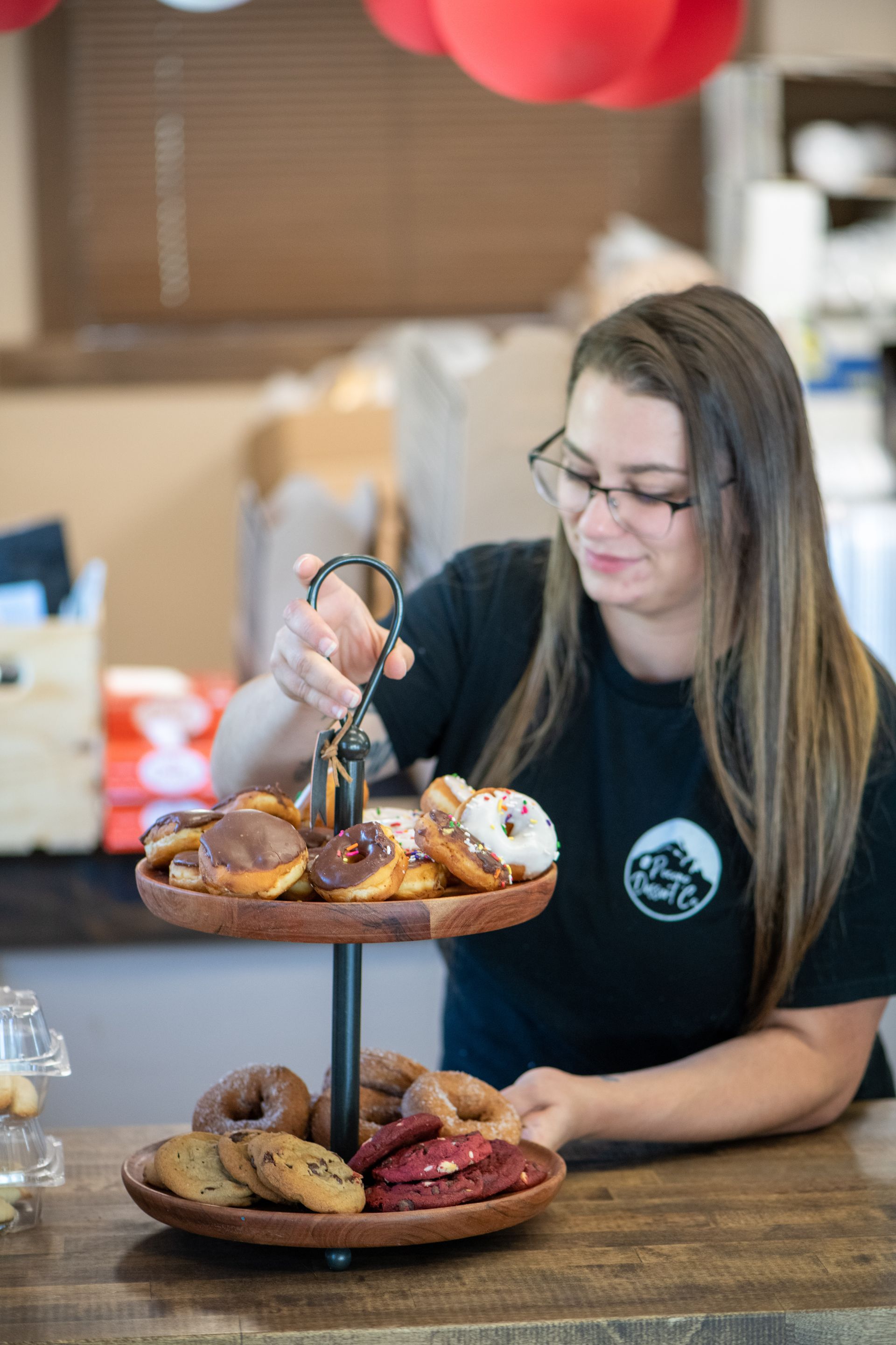 A woman is standing at a counter holding a tray of donuts and cookies.