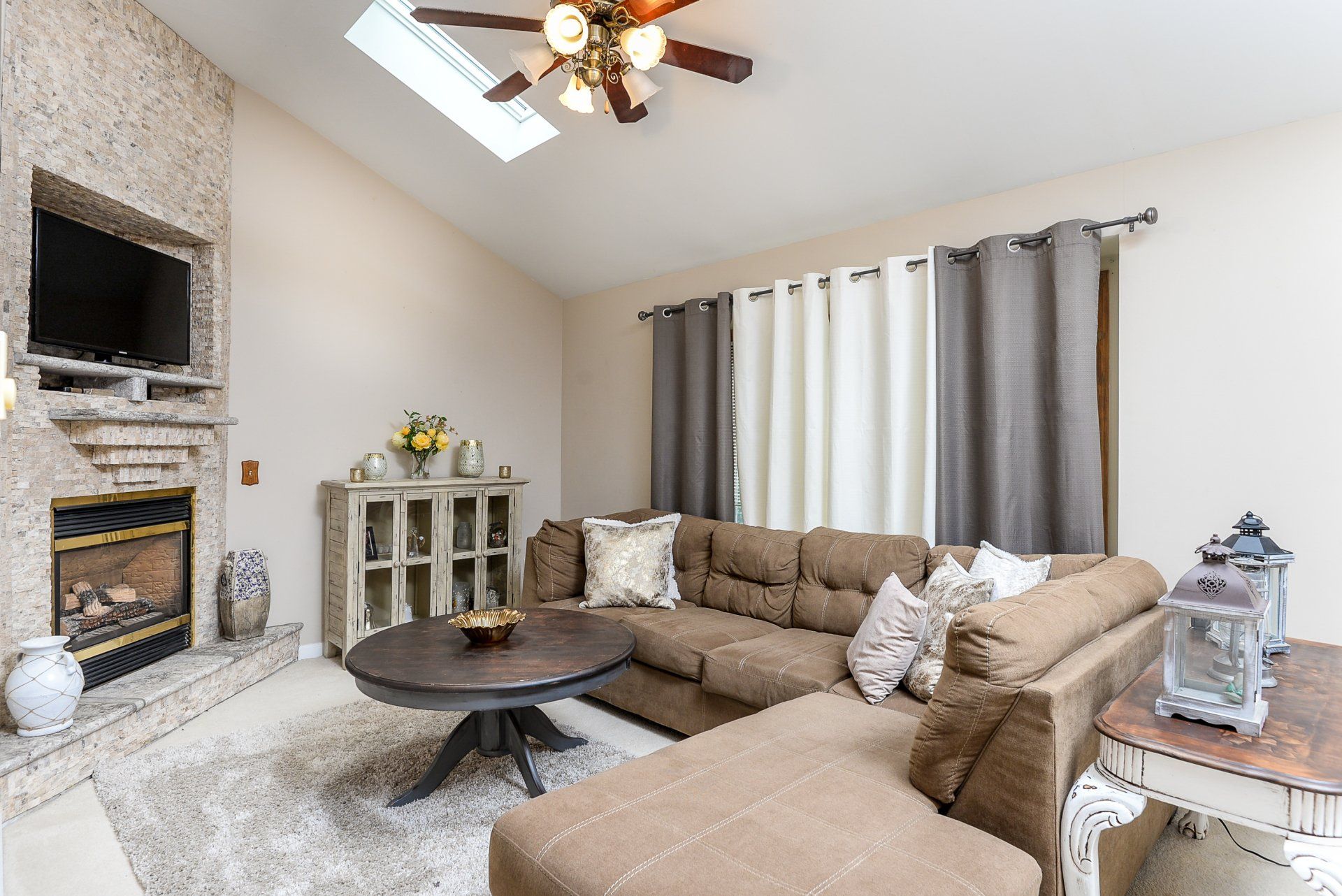 A living room with a couch , fireplace , television and ceiling fan.