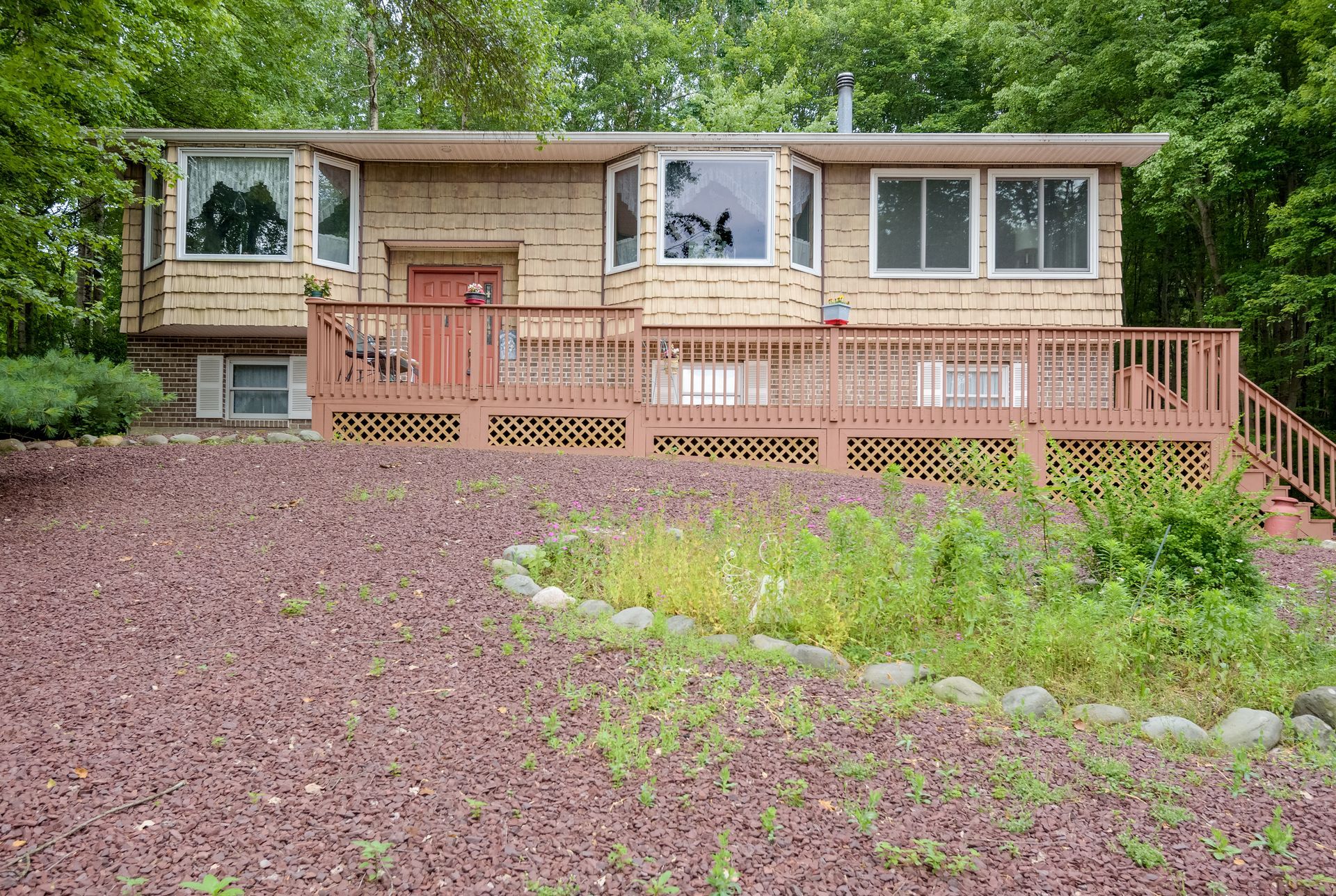 A house with a large deck is sitting on top of a hill surrounded by trees.