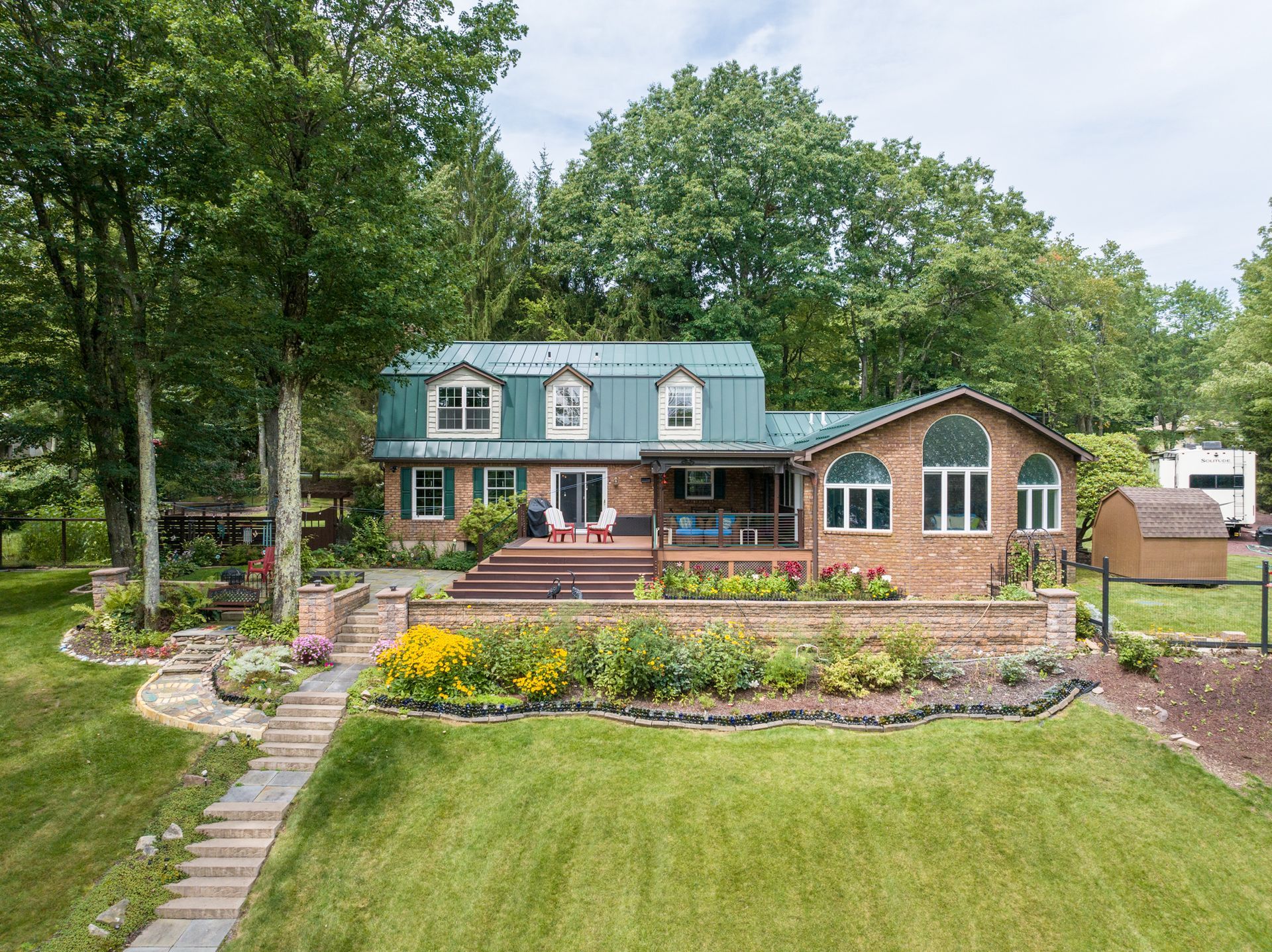 An aerial view of a large brick house with a green roof surrounded by trees.