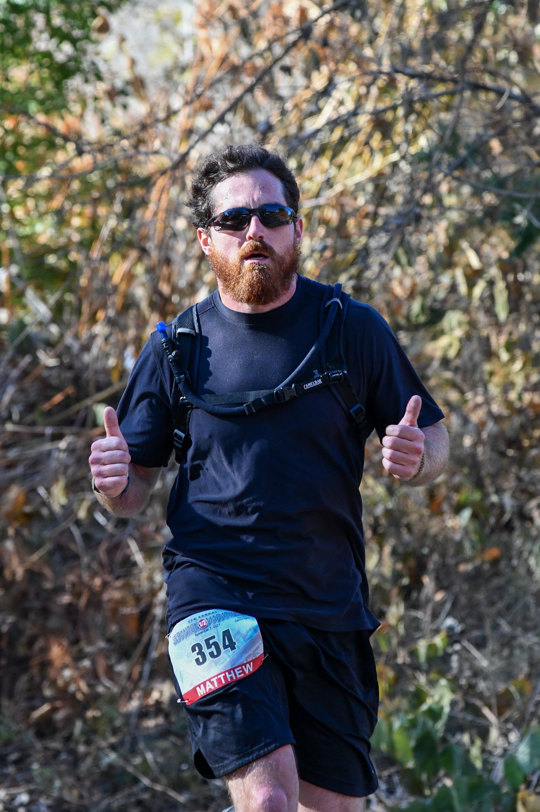 A man with a beard is running in a race and giving a thumbs up.