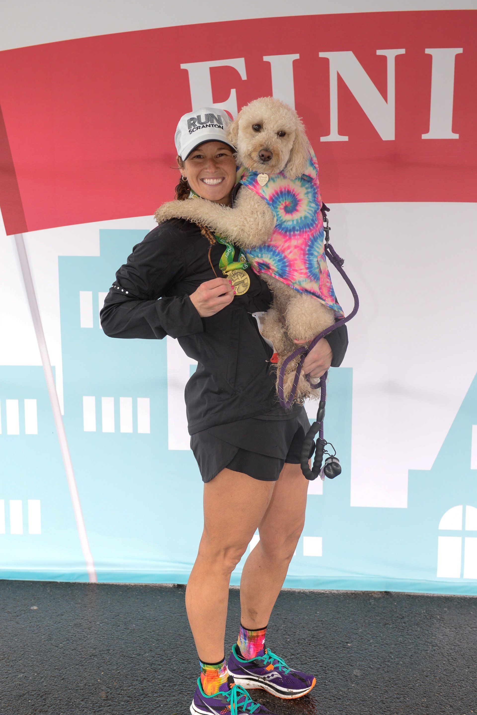 A woman is holding a small dog in front of a sign that says finish