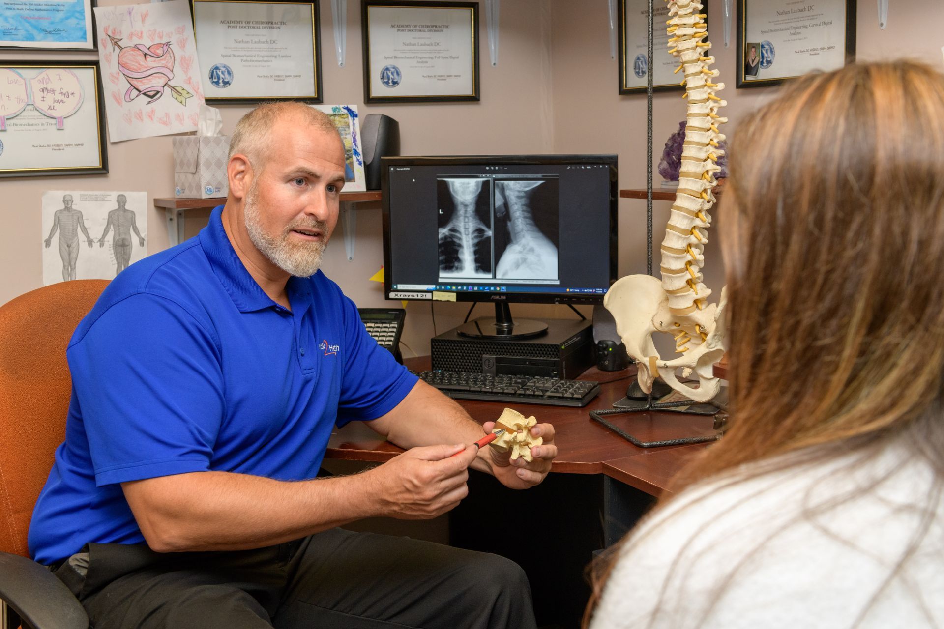 A man is holding a model of a spine while talking to a woman.