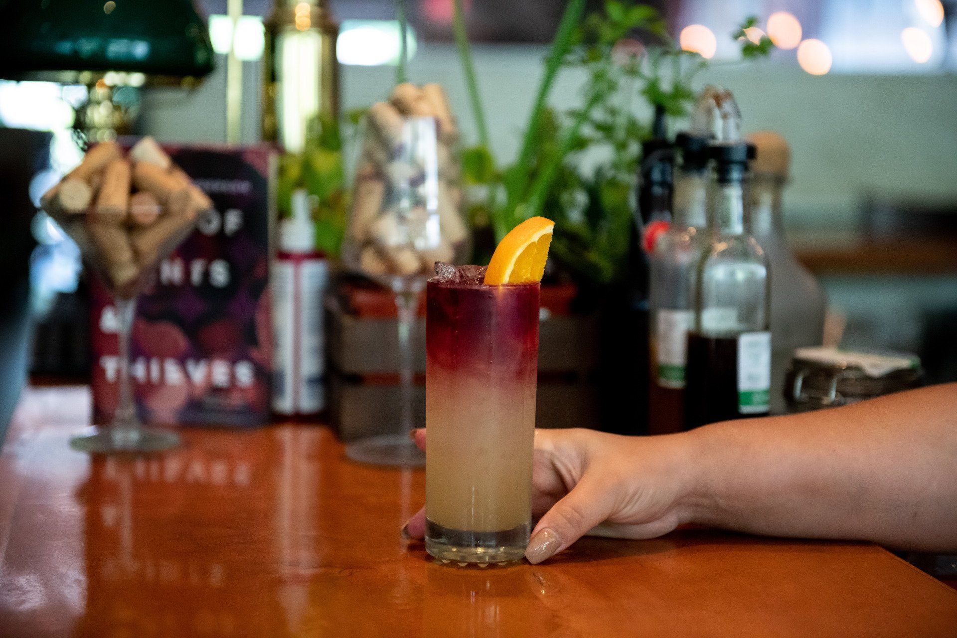 A person is holding a glass of drink on a bar.
