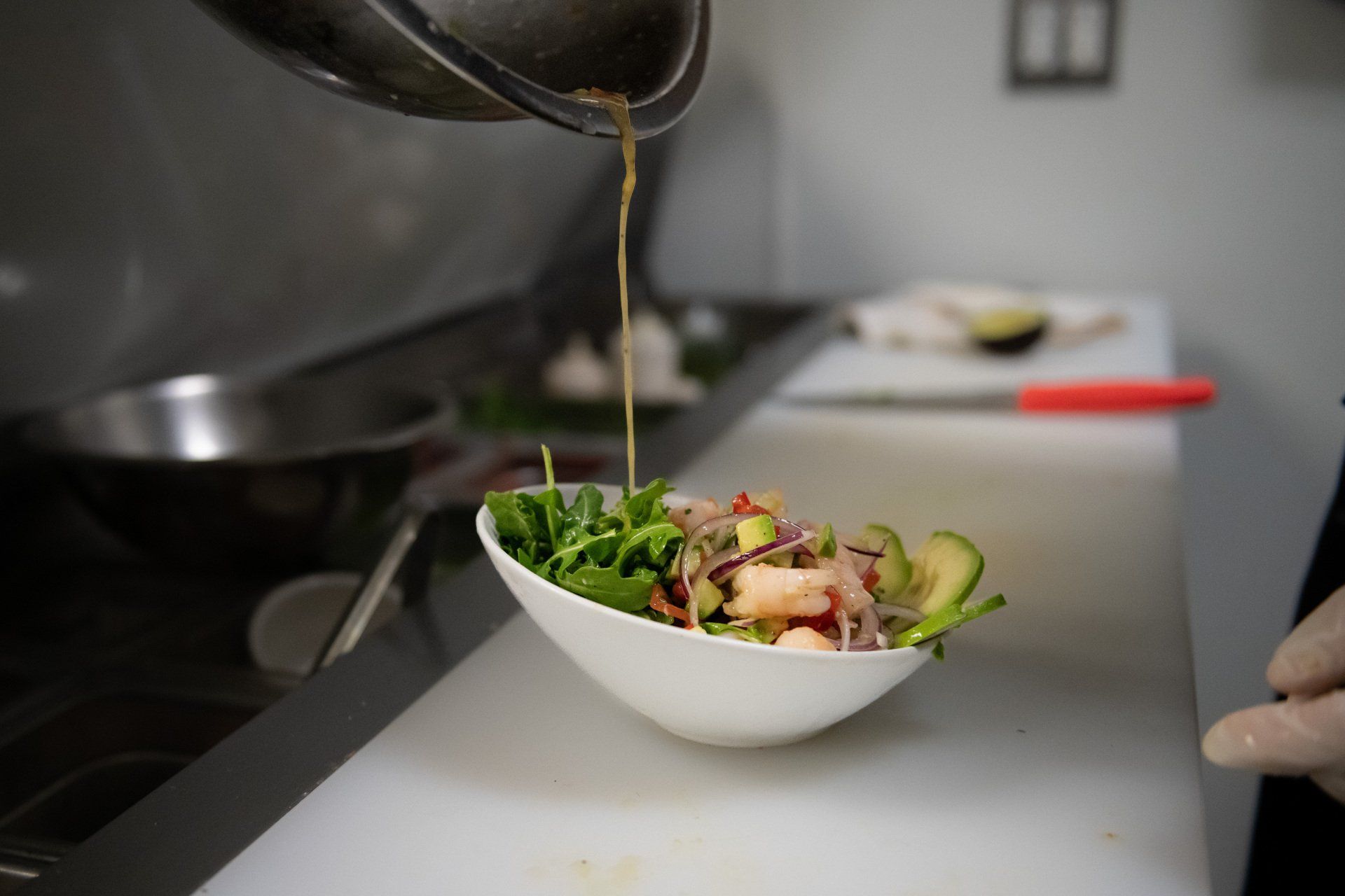 A person is pouring sauce on a salad in a bowl.