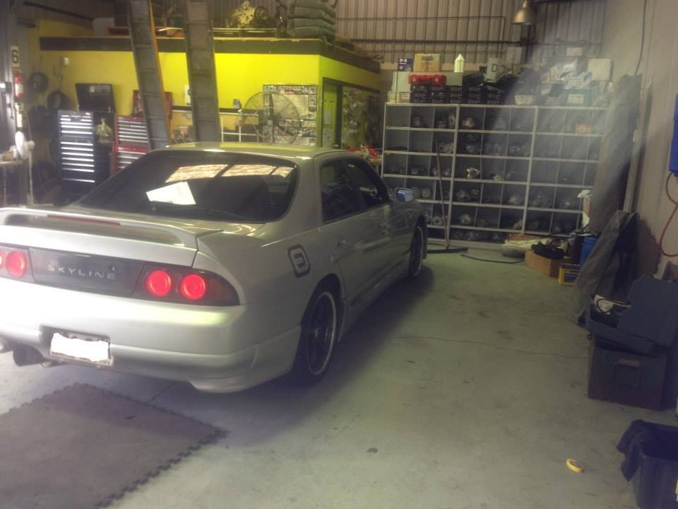 Silver Nissan Skyline parked inside a cluttered garage with shelving and tools; a yellow wall in the background. — Mechanic in Regents Park, QLD