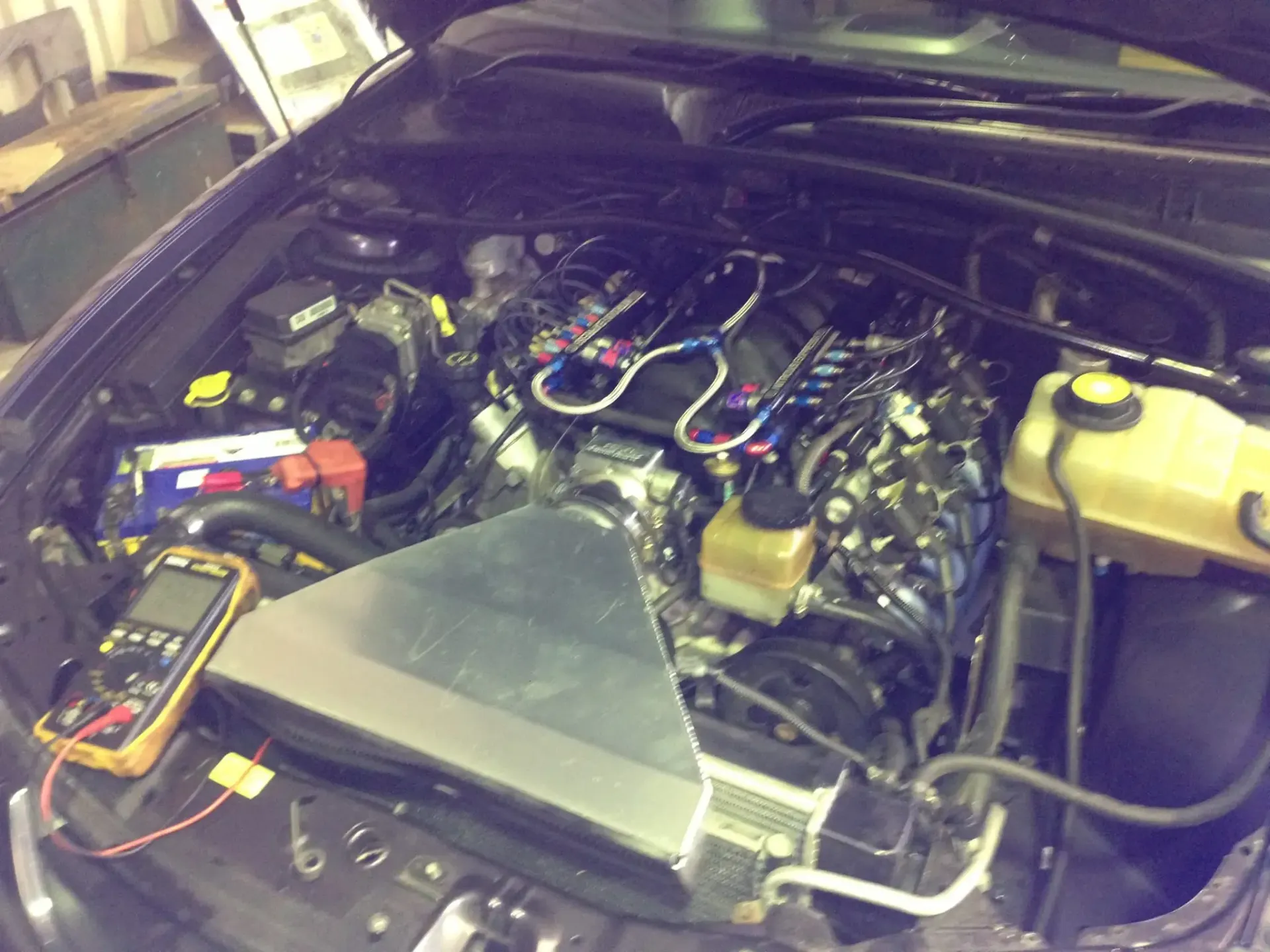 Car engine bay with an engine undergoing diagnostics, multimeter visible.  — Mechanic in Port Macquarie, NSW