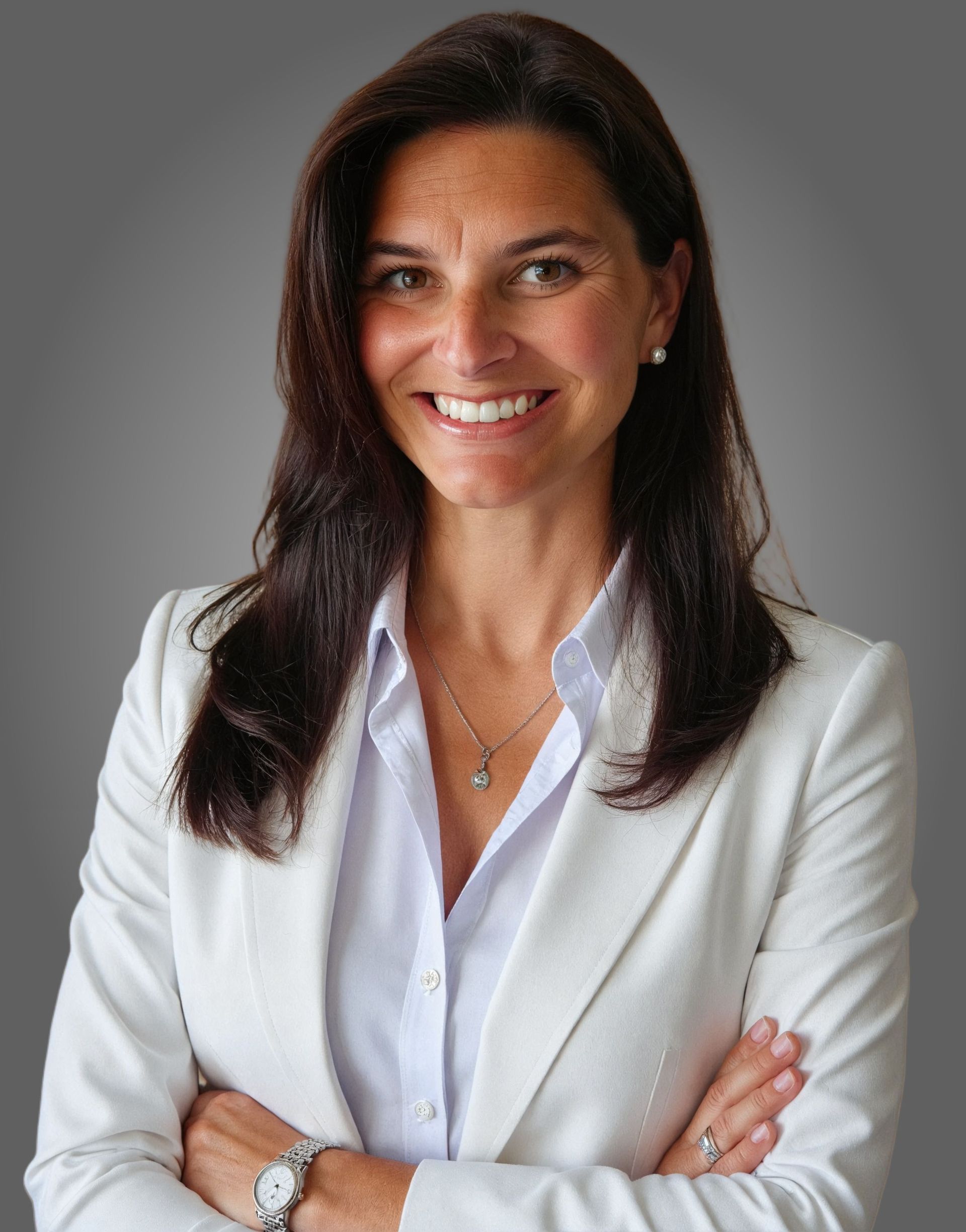 Woman with dark hair, white blazer, arms crossed, smiling, neutral background.