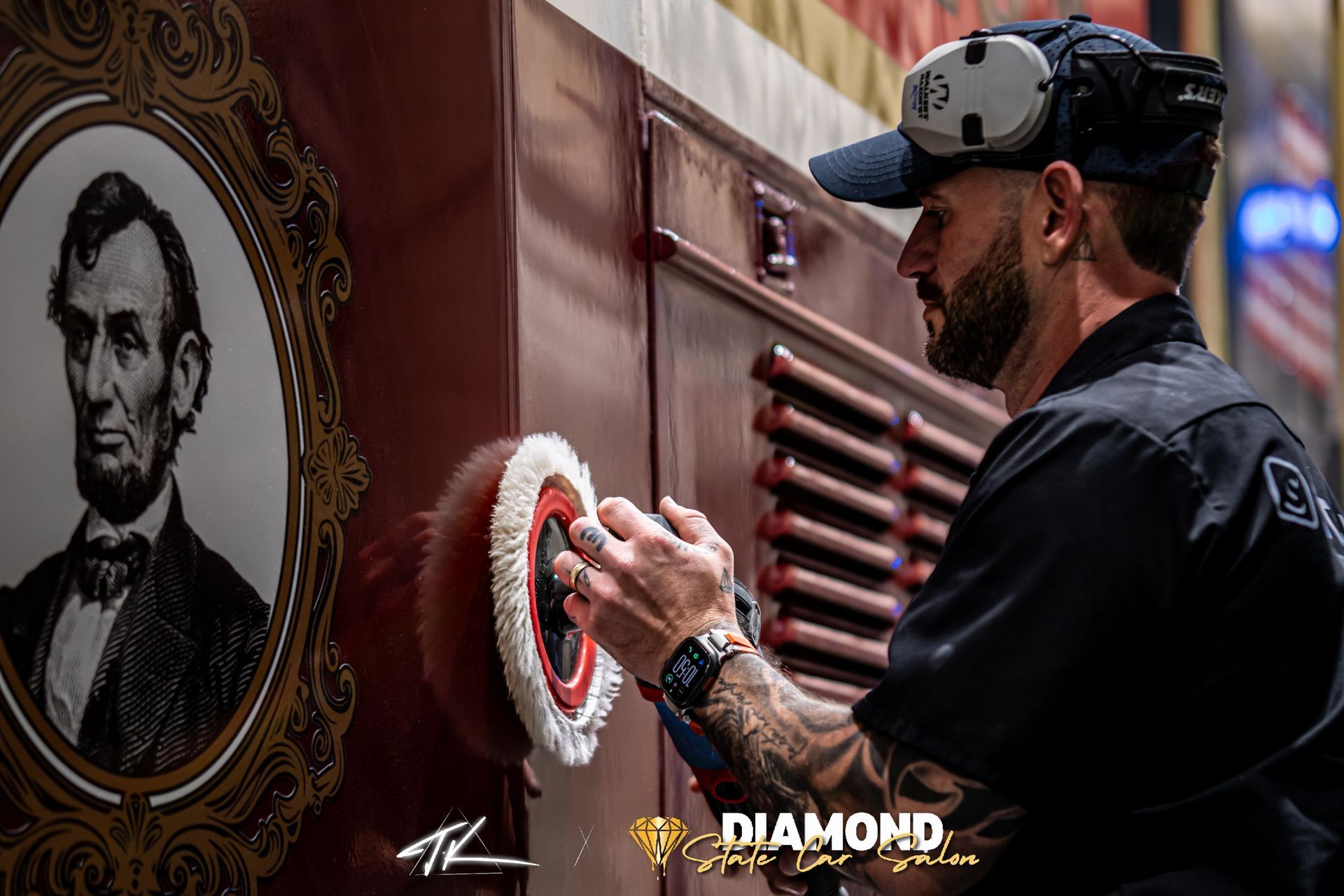 Man buffing a red surface with a polishing tool, a portrait of Abraham Lincoln on the left.