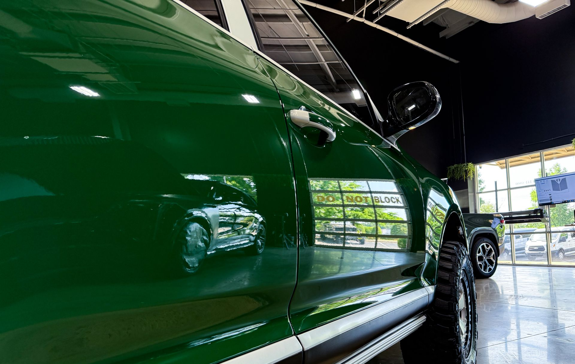 Green off-road Porsche Cayenne SUV with roof rack, spotlights, and rugged tires in a garage.