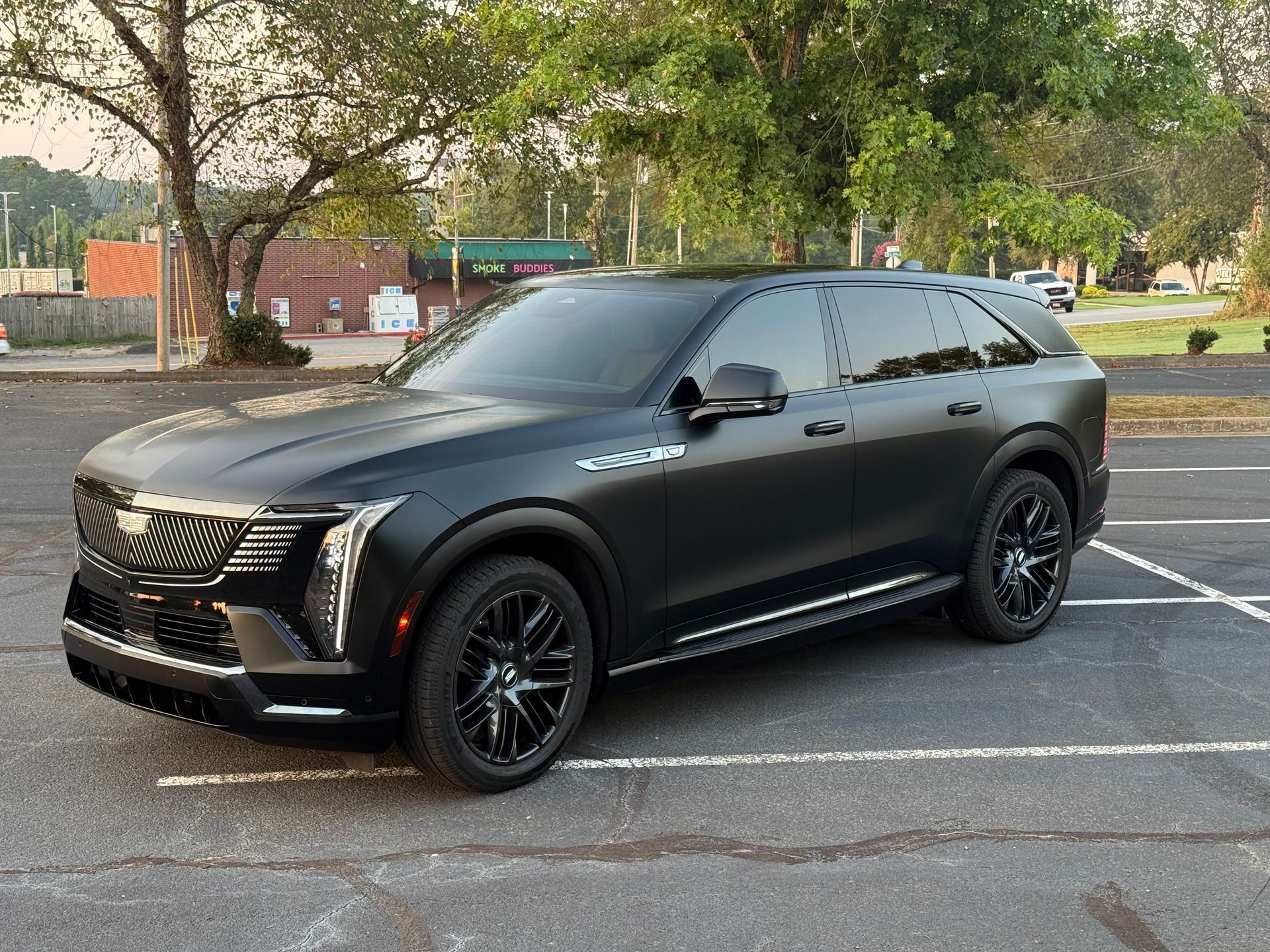 Black Cadillac SUV parked in a lot at sunset, dark tinted windows, black wheels.