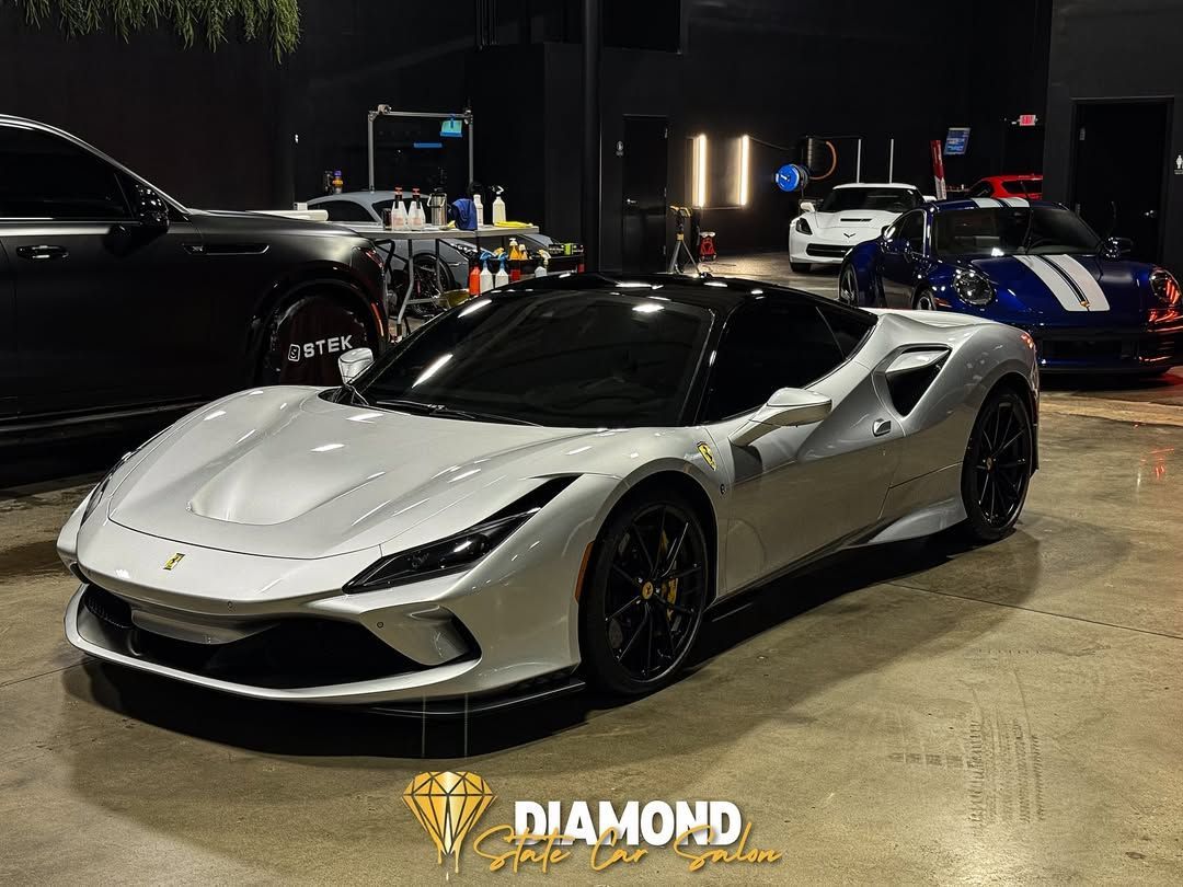 White Ferrari convertible parked inside a detailing shop, other cars in background.