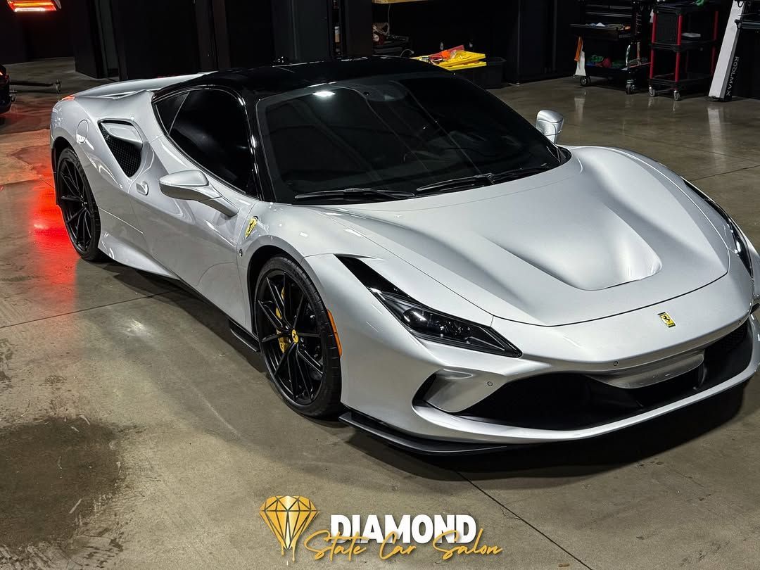 Silver Ferrari sports car with black roof and wheels in a garage.