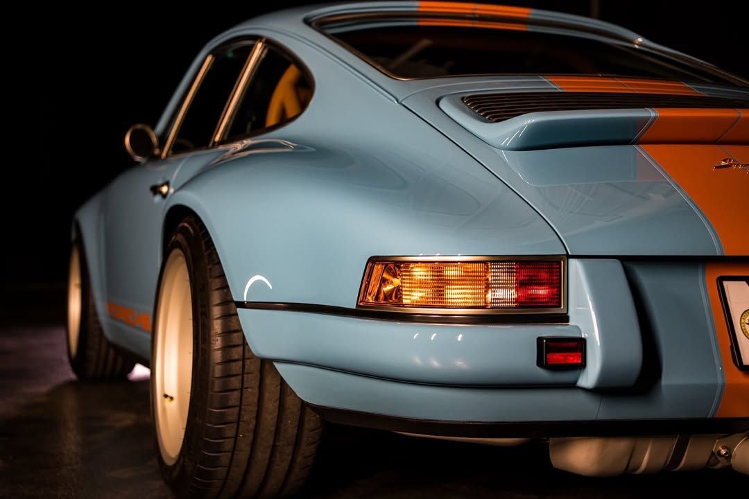 Light blue and orange Porsche 911, rear view, in a dark setting.