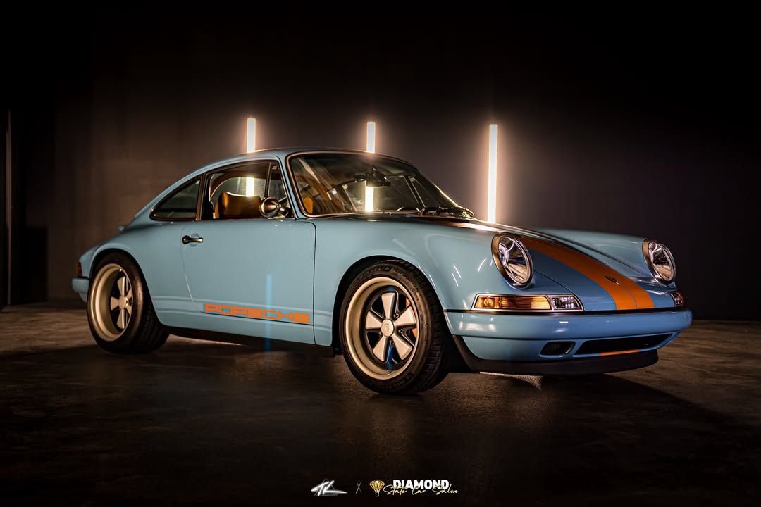 Light blue classic Porsche 911 with orange stripe on a dark background.