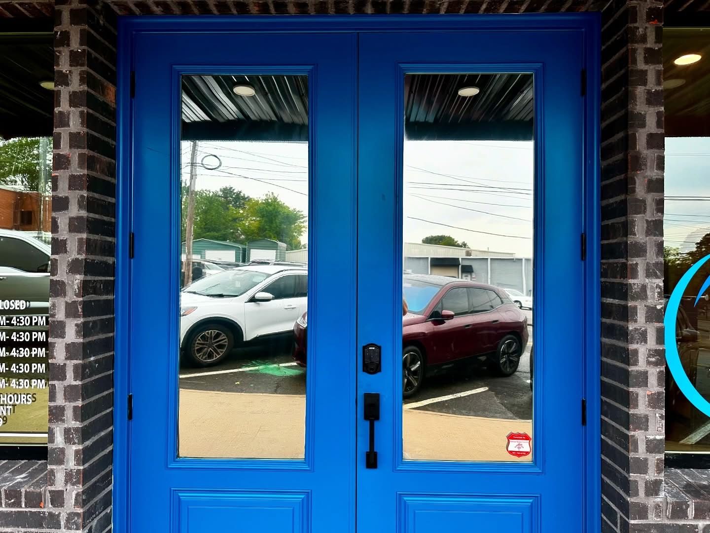 Blue double doors with glass panels reflecting cars, set in a brick facade.