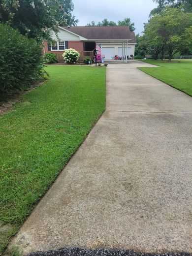 A concrete driveway leading to a house with a lush green lawn.