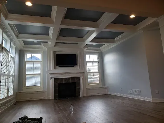 Living room with gray coffered ceiling, fireplace, windows, and wood flooring.