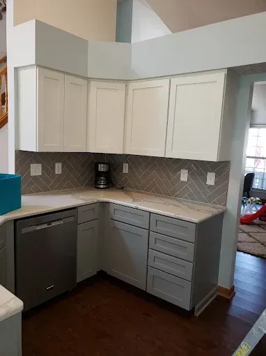 A renovated kitchen with white upper cabinets, gray lower cabinets, and a gray herringbone backsplash.