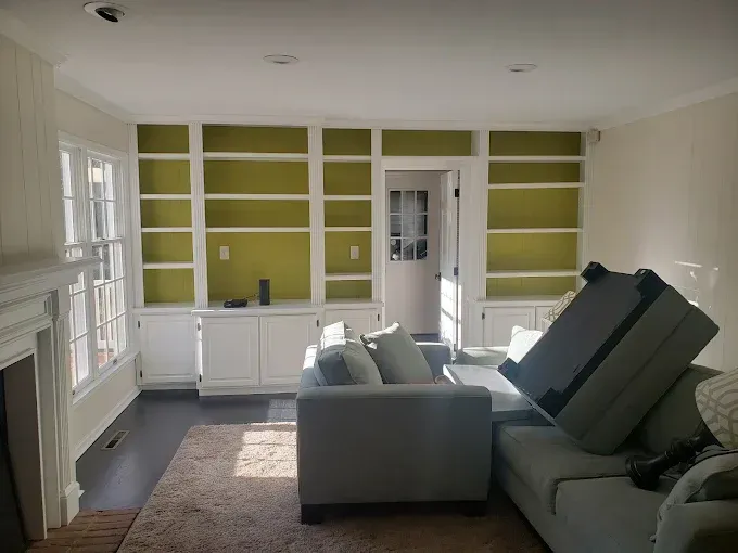 Living room with built-in bookshelves painted olive green, white trim, gray sofa, dark wood floor.