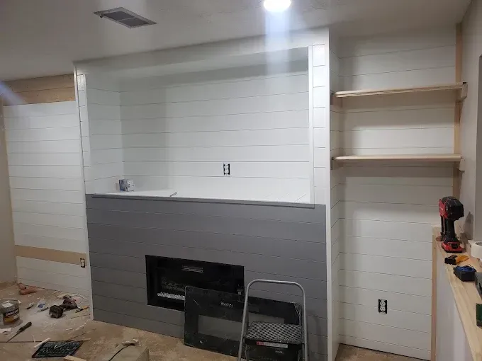 Fireplace and shelves under construction, walls are white shiplap, bottom portion gray.
