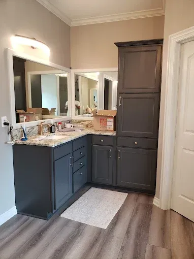 Gray bathroom vanity with storage cabinets and a mirror, with a white rug.