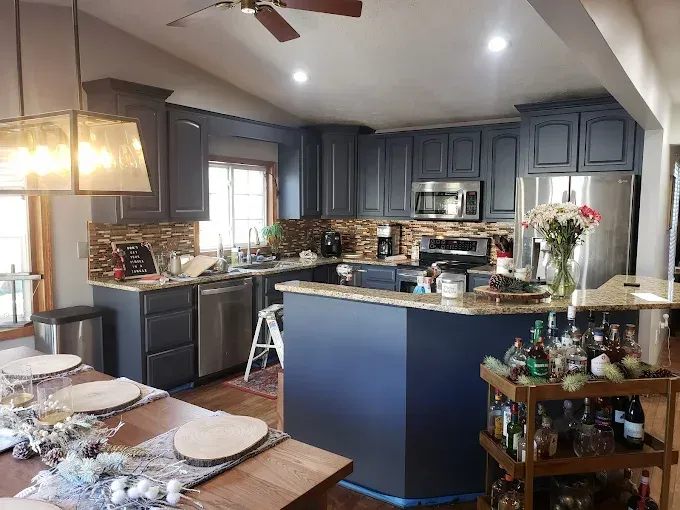 Blue kitchen with island, stainless steel appliances, and wood dining table with place settings.