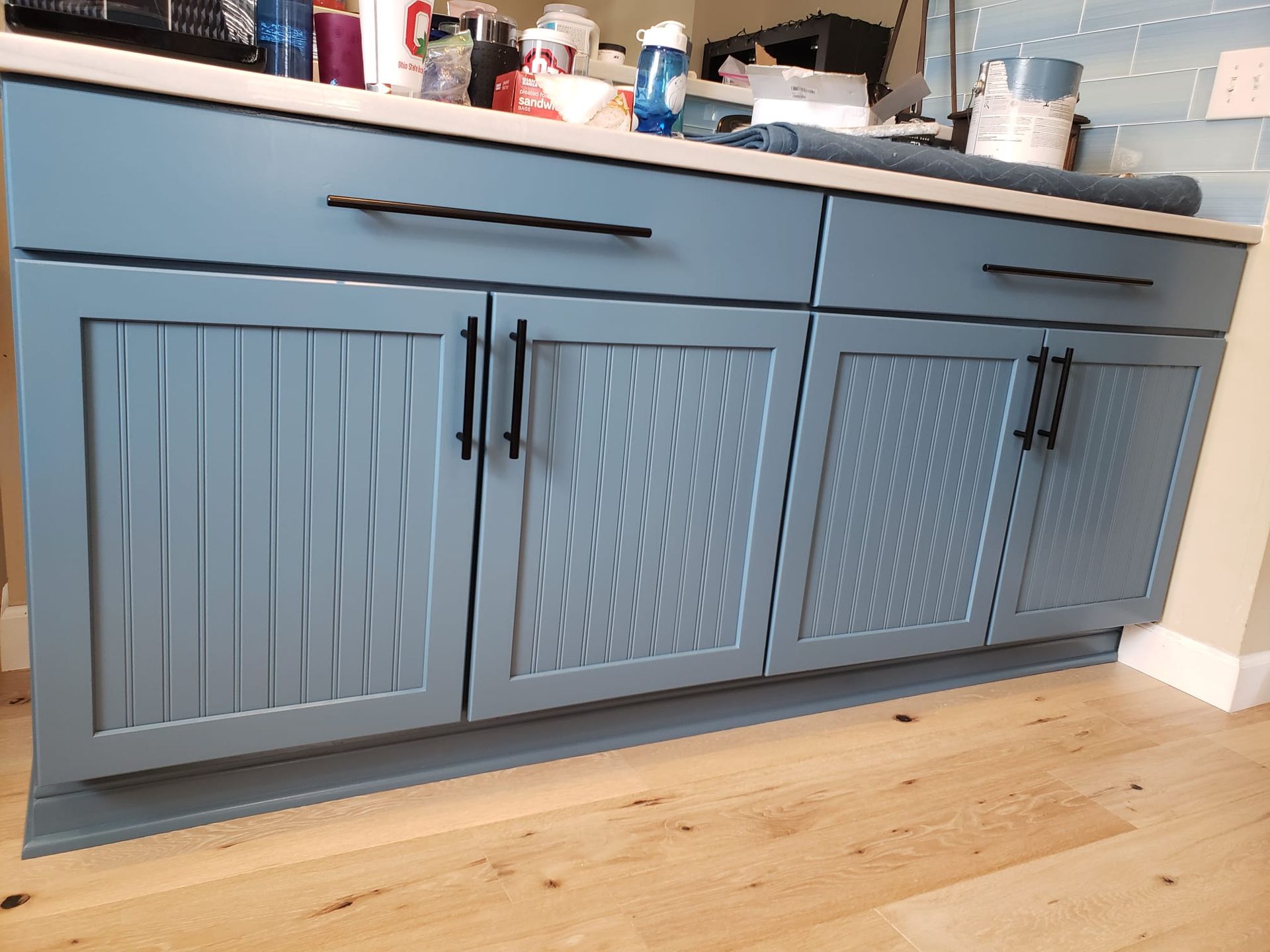 Blue kitchen cabinets with textured doors and black handles, beneath a white countertop.