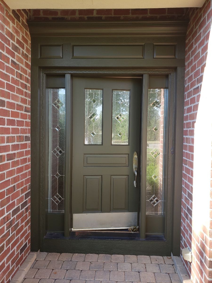 Olive green front door with sidelights, set in a brick facade.
