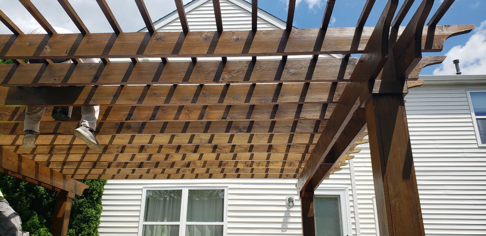 Wooden pergola with a white house in the background and a blue sky overhead.