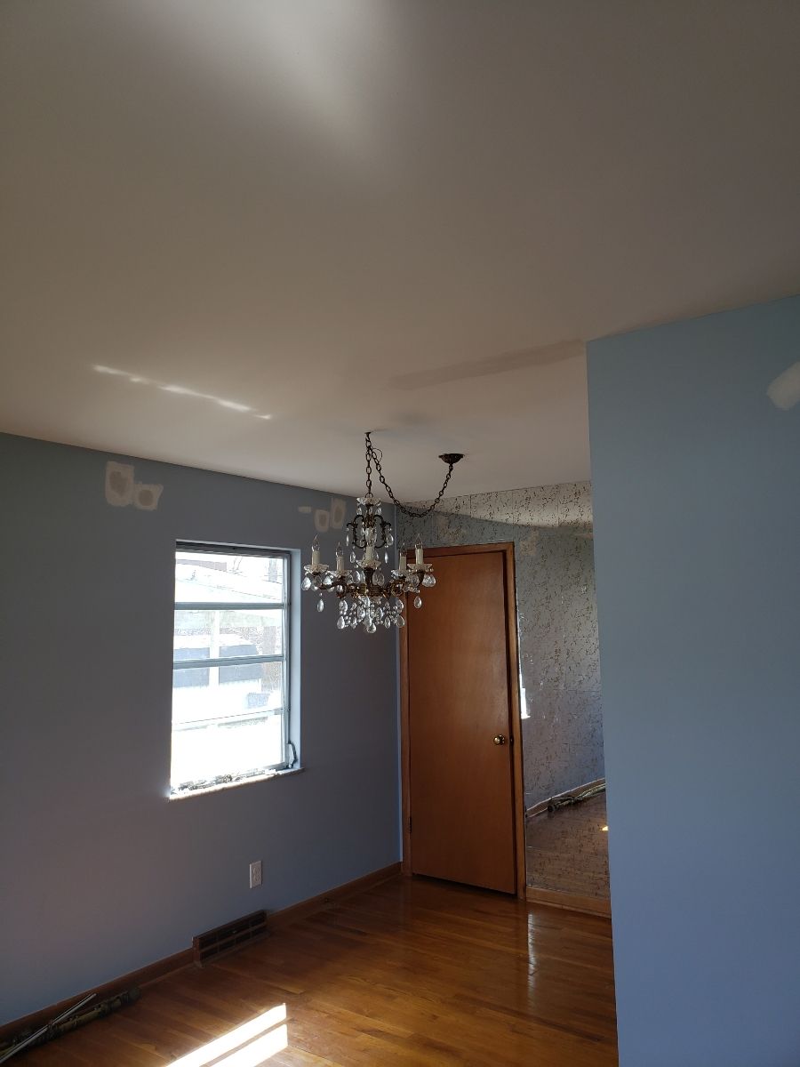 Dining room with light blue walls, wood floor, chandelier, and a brown door.