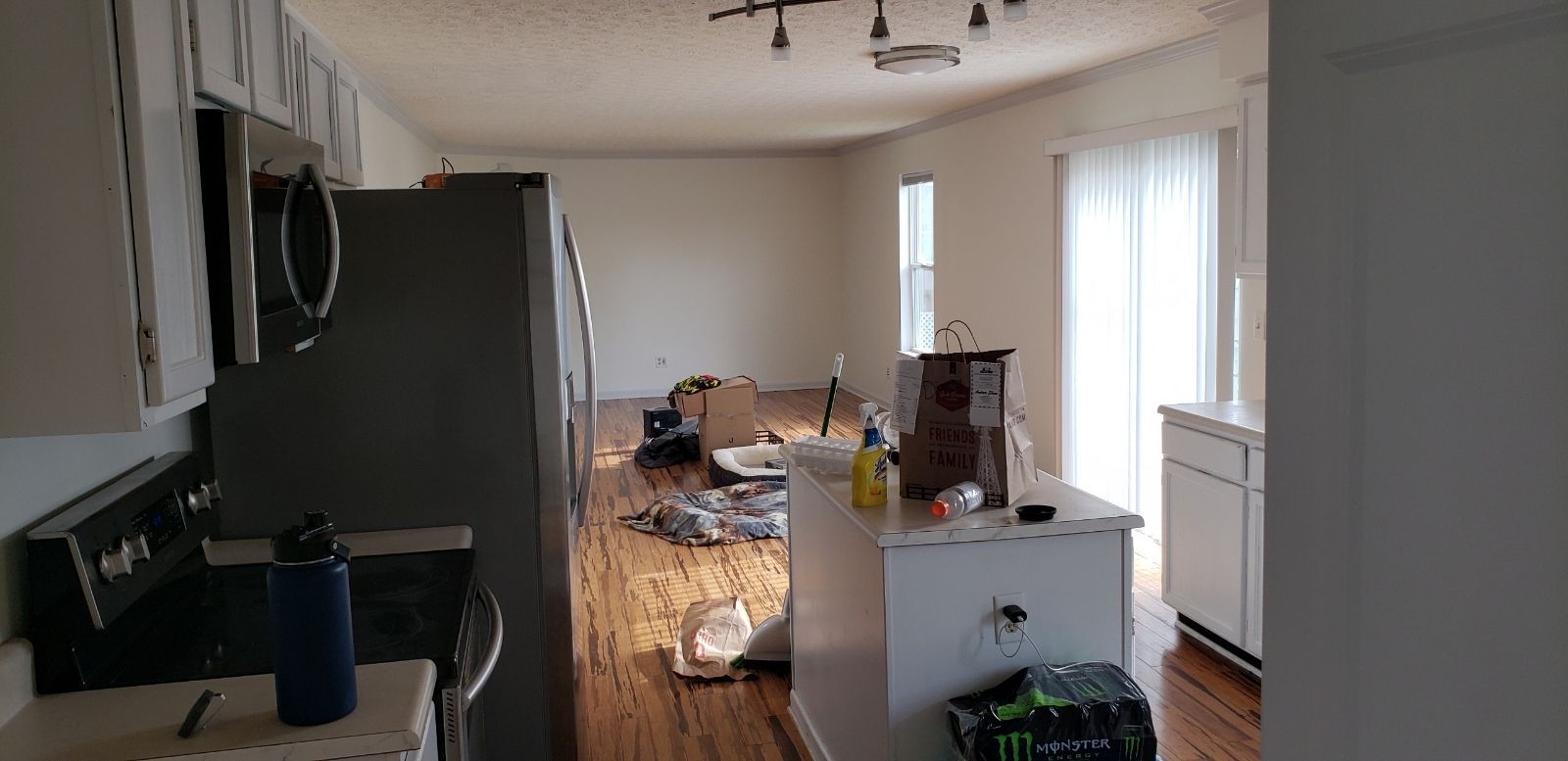 Kitchen with refrigerator, stove, island, and open living space. Window with sheer curtains on the right.