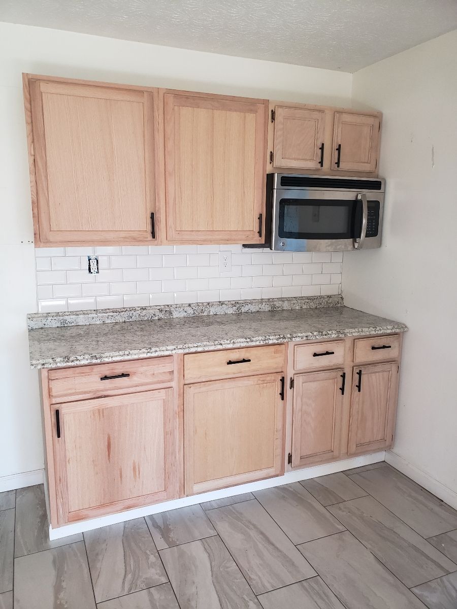 Kitchen with light wood cabinets, gray countertop, white tile backsplash, and microwave.
