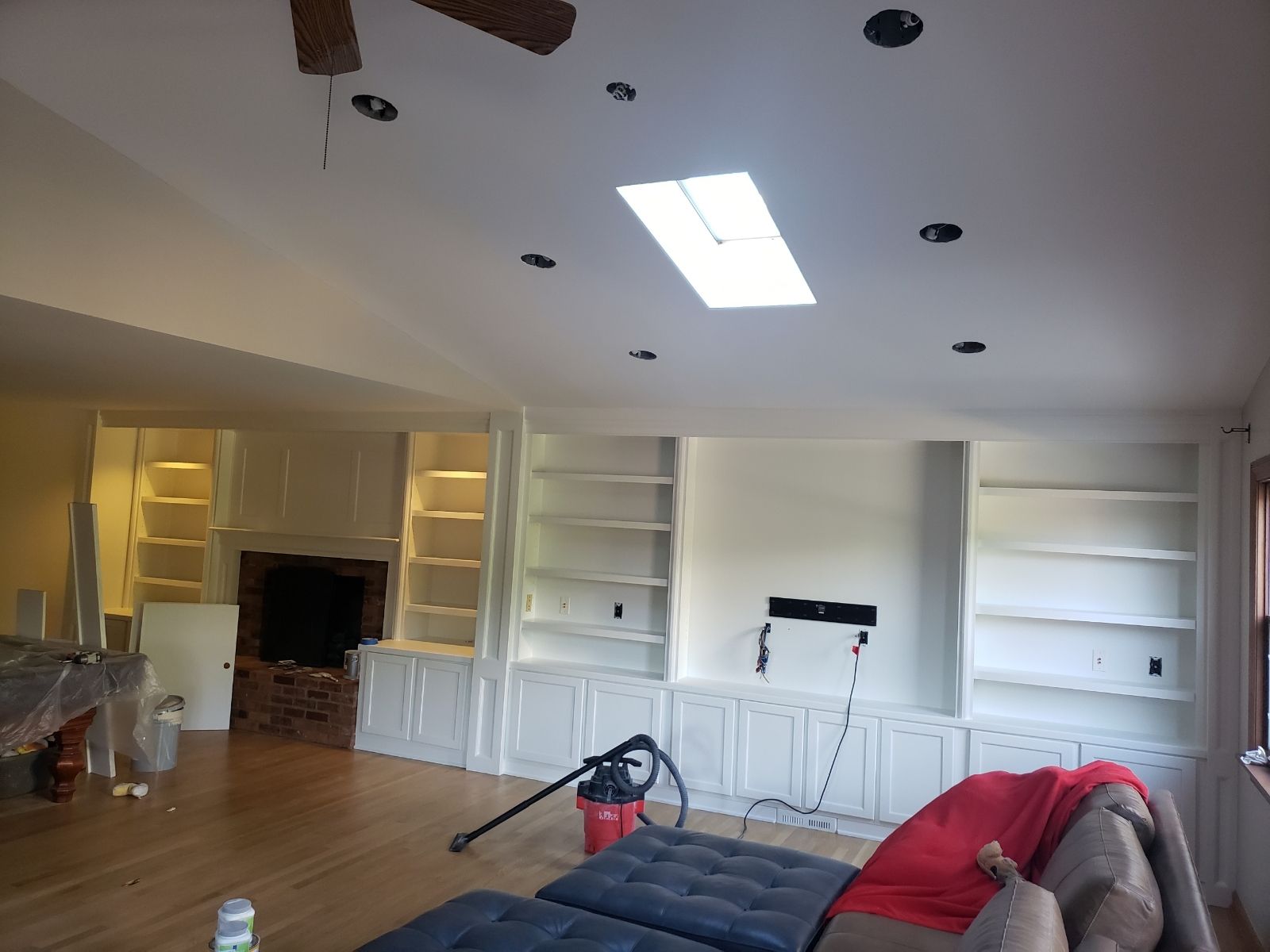 Interior view of a living room with built-in white bookshelves, recessed lighting, and skylight. Hardwood floor.