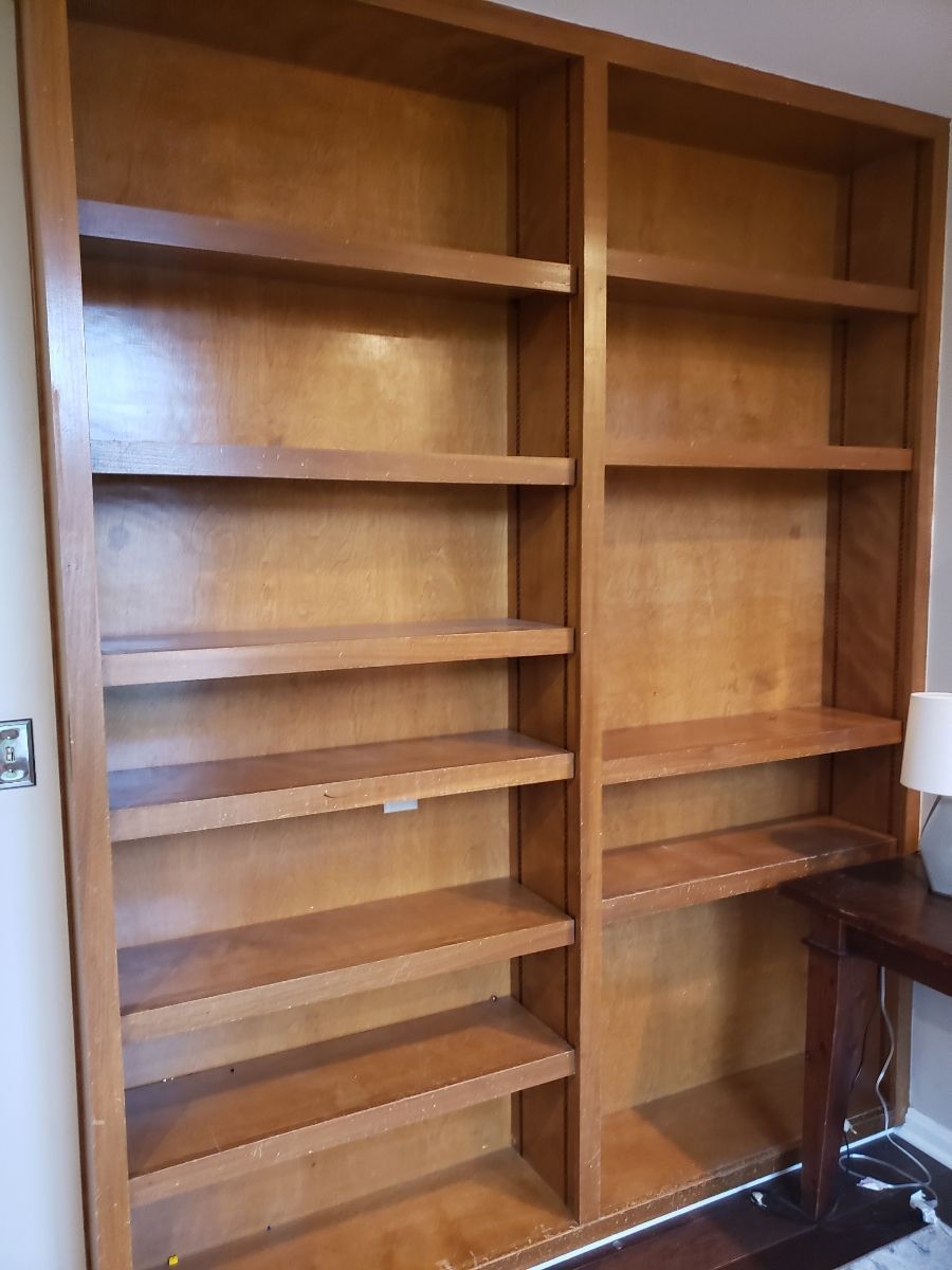 Wooden built-in bookshelves with several shelves; brown color; next to a small table with a lamp.