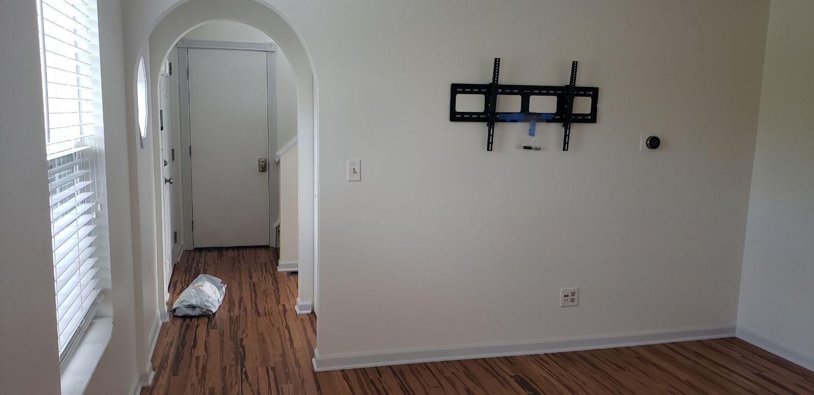 Interior view of a room with hardwood floors, white walls, and a mounted TV bracket.