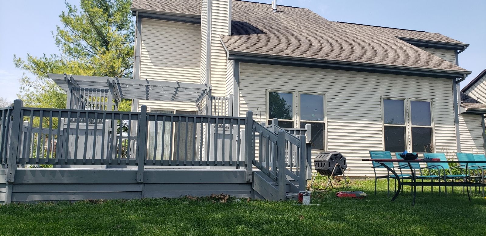 Backyard with gray deck, siding house, and blue table and chairs on the grass.