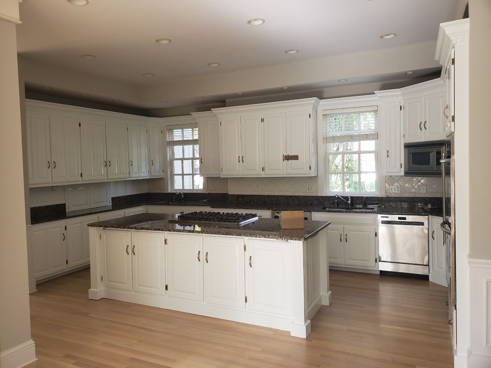 White kitchen with dark countertops and island. Stainless steel appliances and light wood floors.