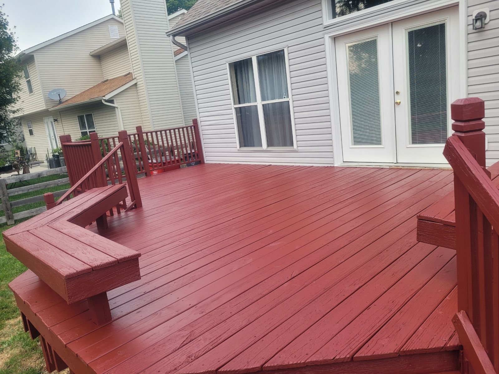 Red-painted wooden deck with built-in seating, railings, and French doors leading into a light-colored building.