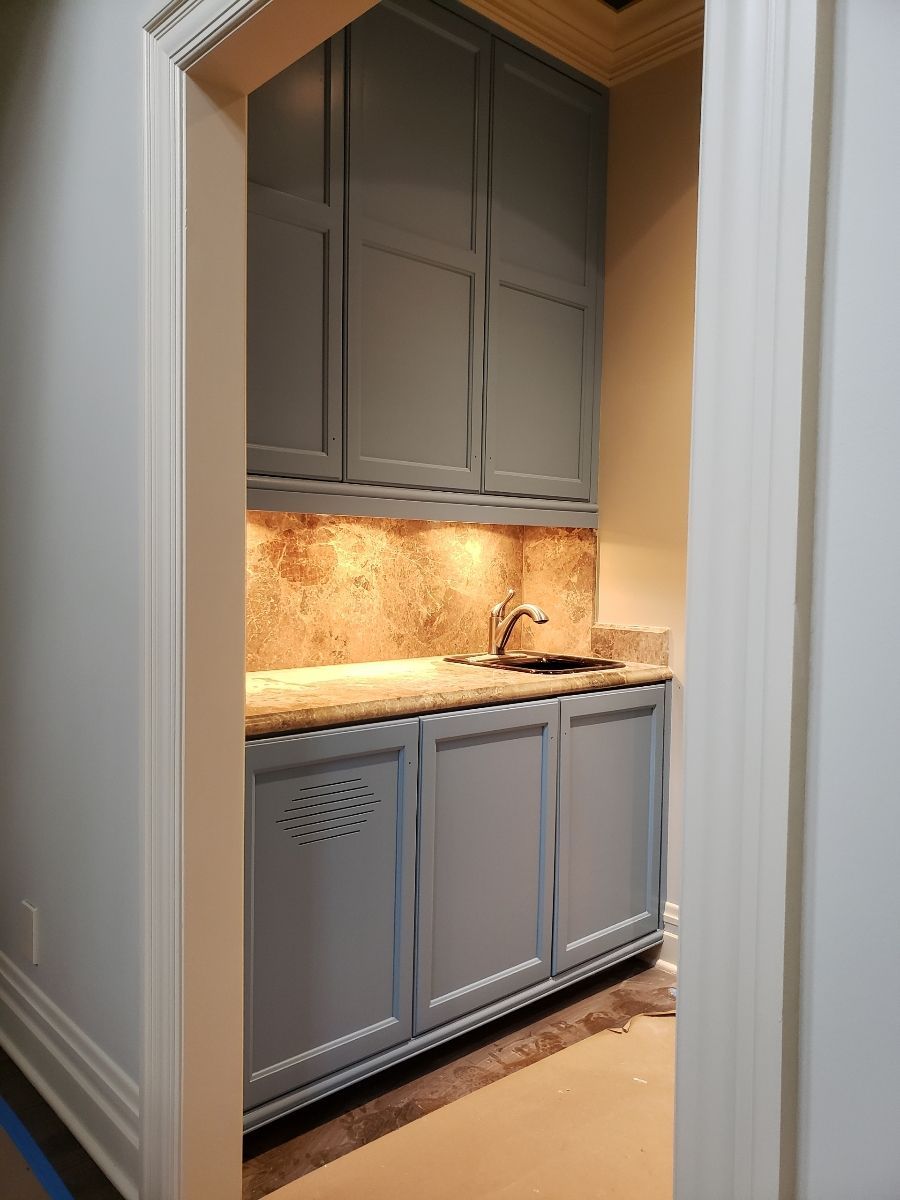 Blue cabinets with sink, backsplash, and upper storage in a doorway setting.