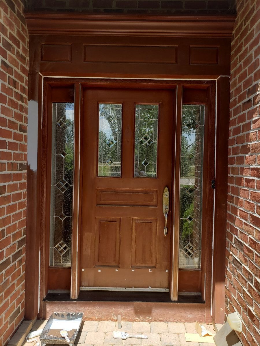 Wooden front door with glass sidelights and transom, set in a brick wall.