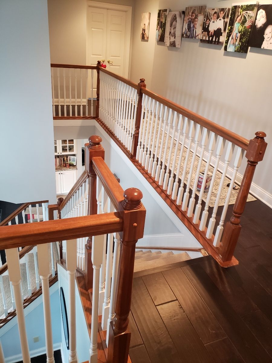 Staircase with wooden handrails and white spindles, leading to a hallway with artwork.