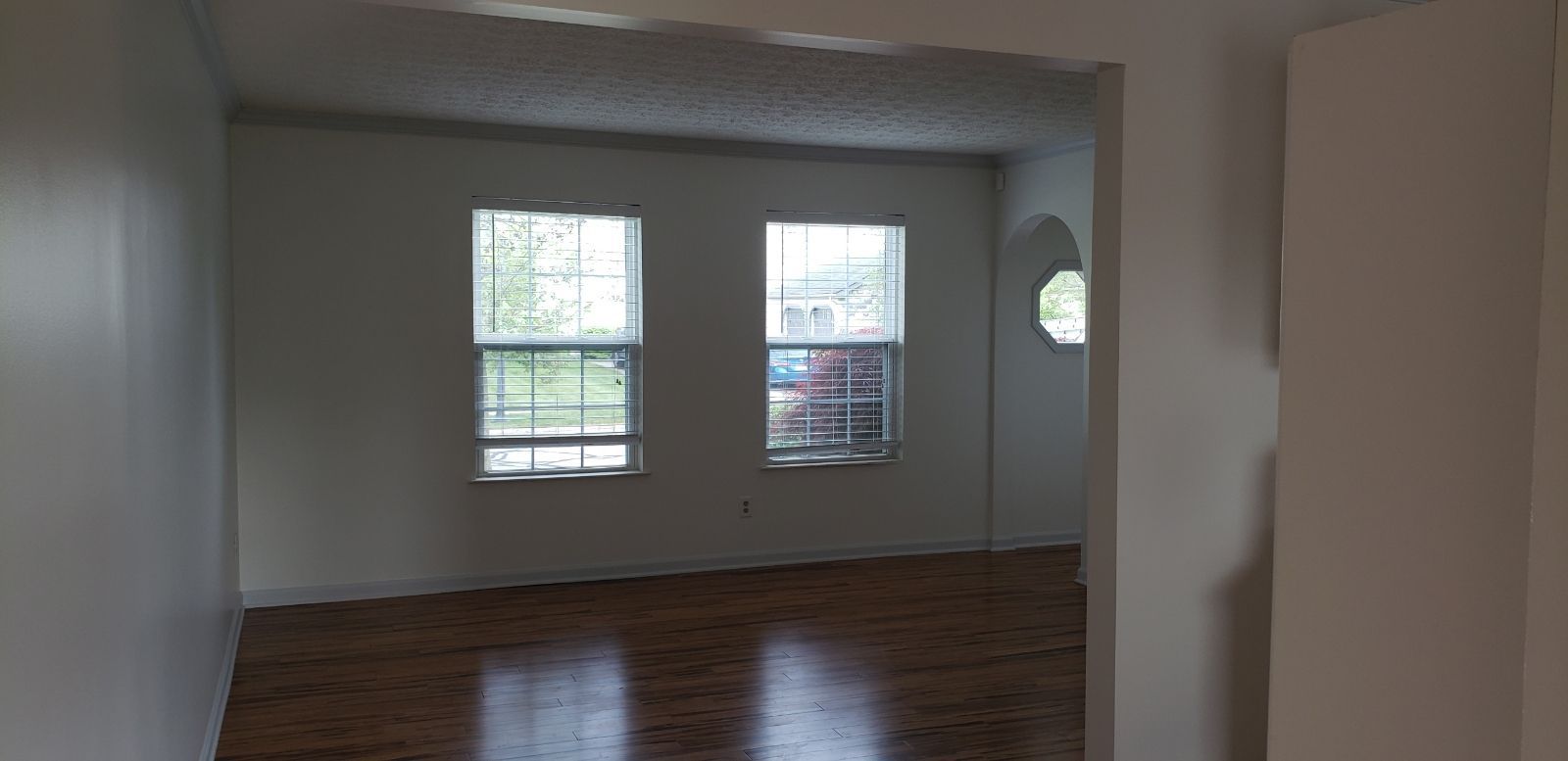 Interior view of a room with two windows and a round window. The floor is hardwood.