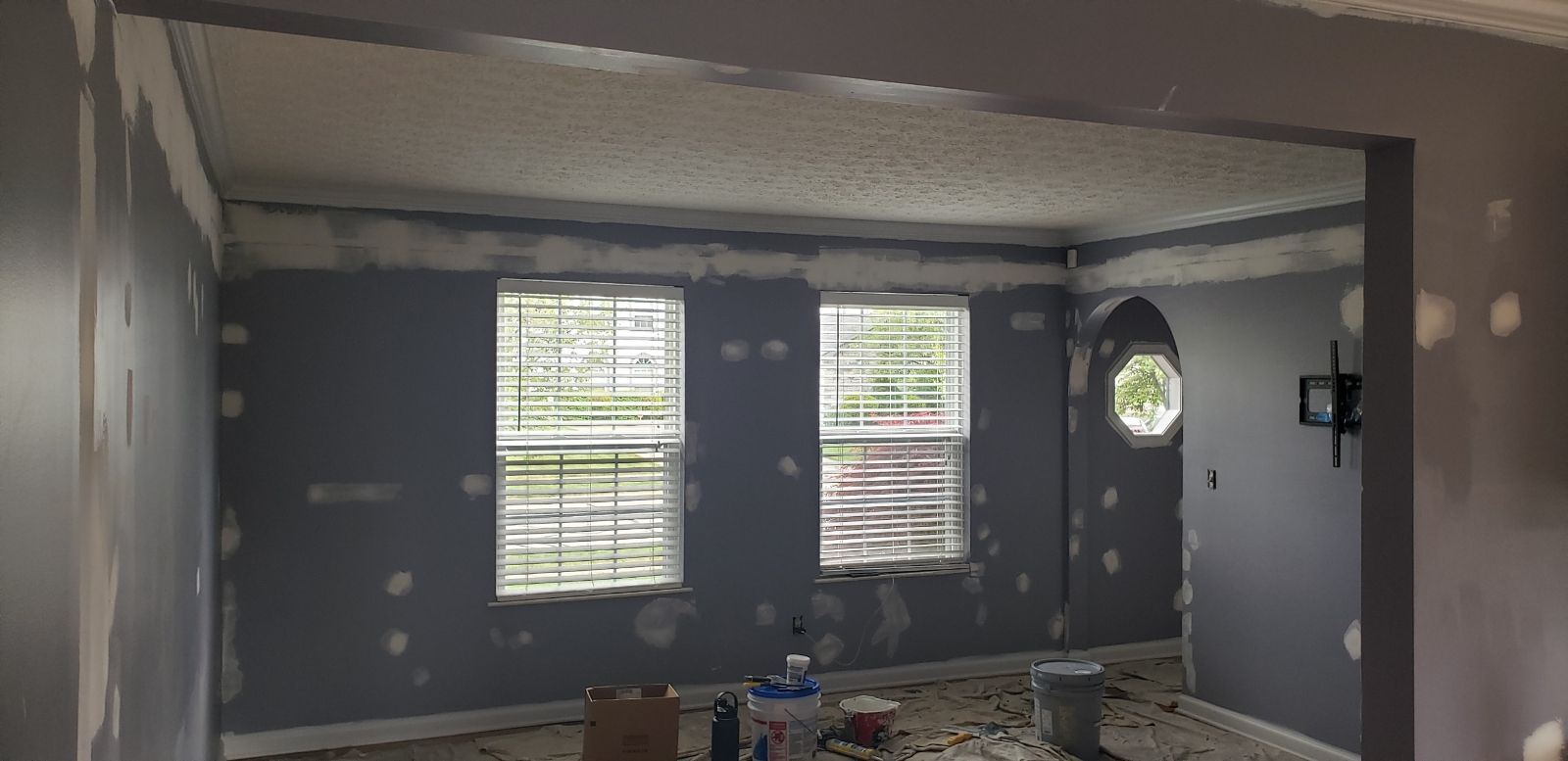 Interior room with two windows and a round window. Walls are painted gray, with plaster patches.