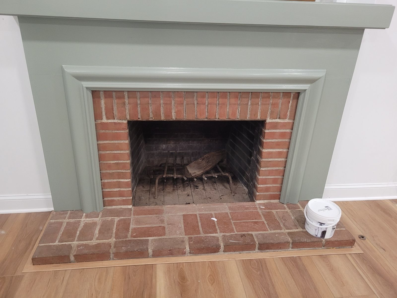 Brick fireplace with a painted green mantel, on a wood floor.