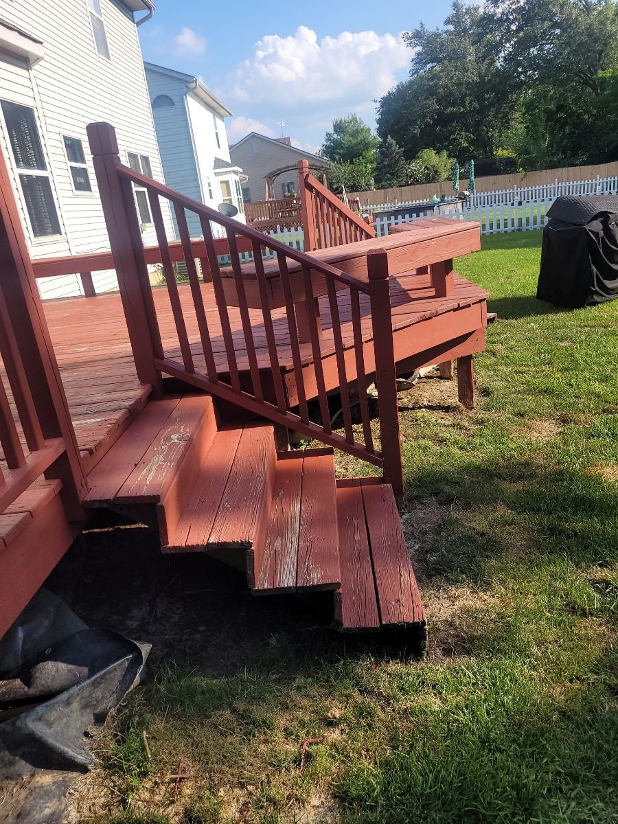 Red wooden deck and steps leading to a backyard with grass and white fence.