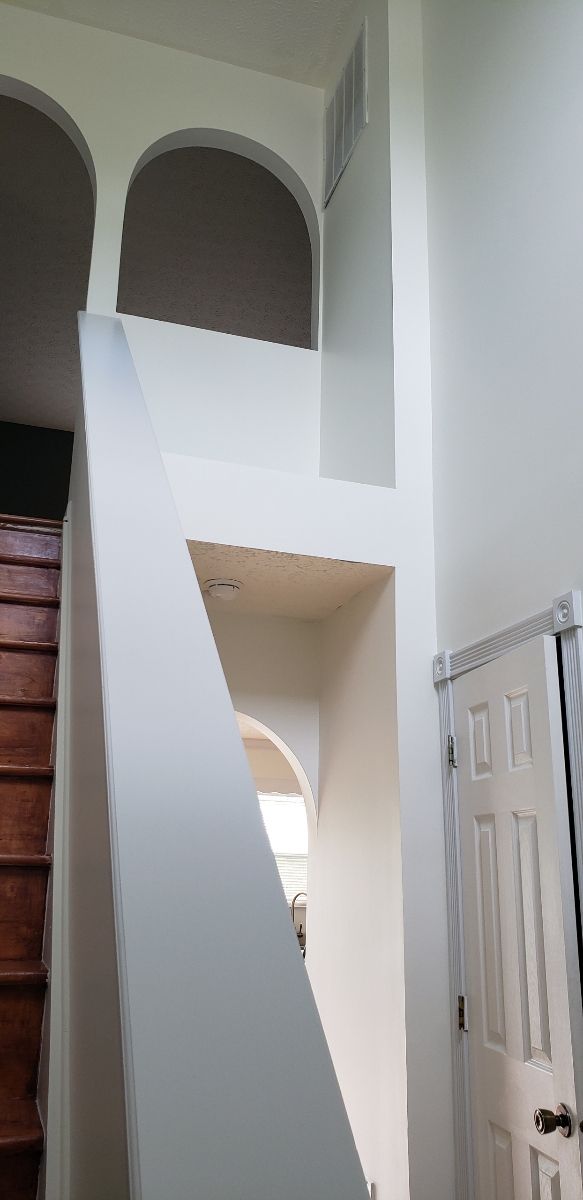 Interior with a staircase, arches, and a door, painted in white and neutral tones.
