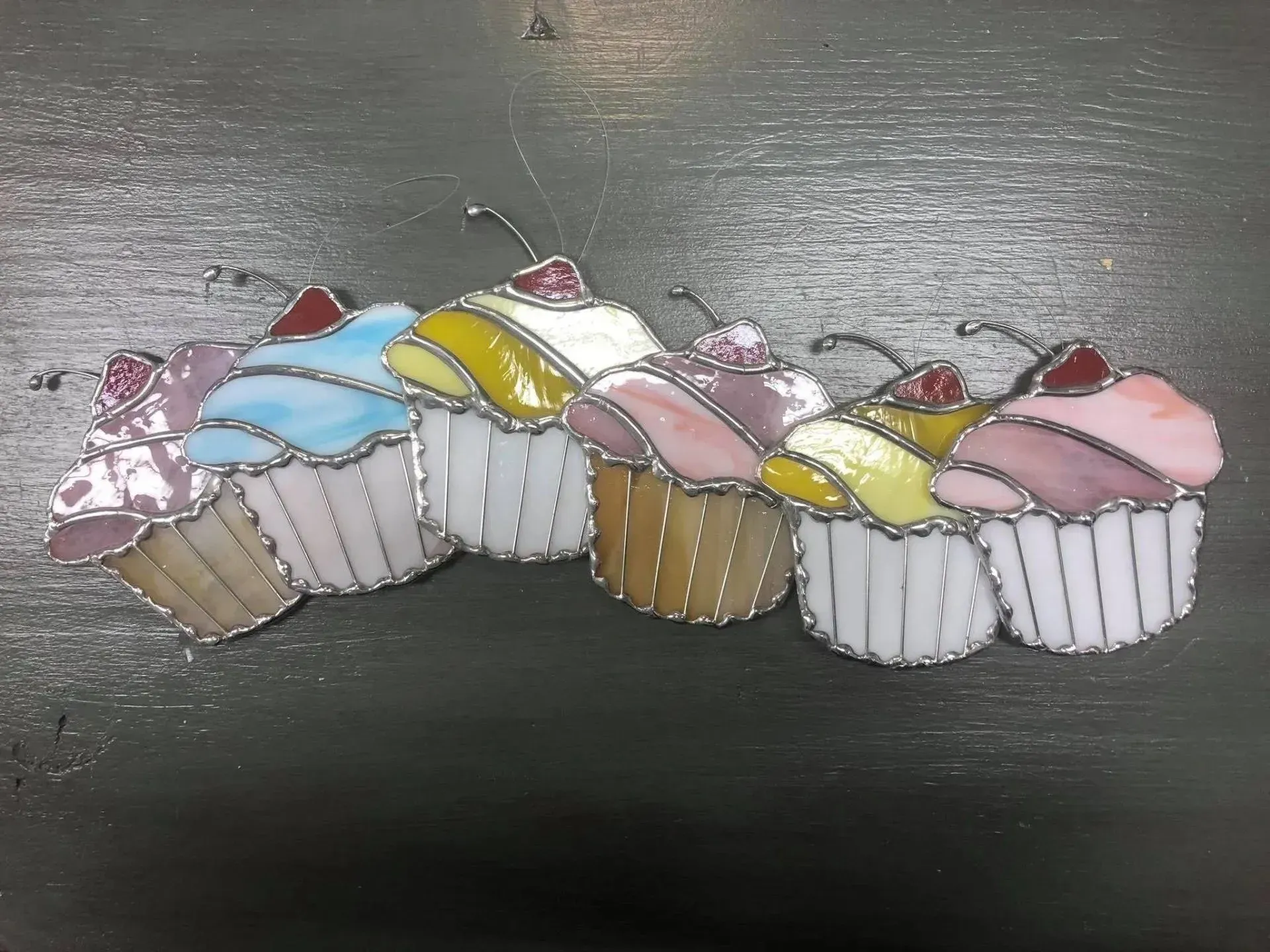 Stained glass cupcakes in pastel colors, topped with cherries, resting on a dark surface.