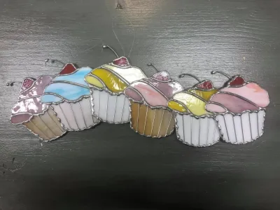Stained glass cupcakes in pastel colors, topped with cherries, resting on a dark surface.