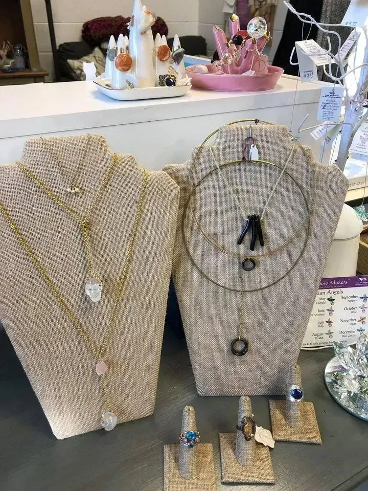 Jewelry display: necklaces and rings on tan fabric stands, set on a counter with other store items in the background.